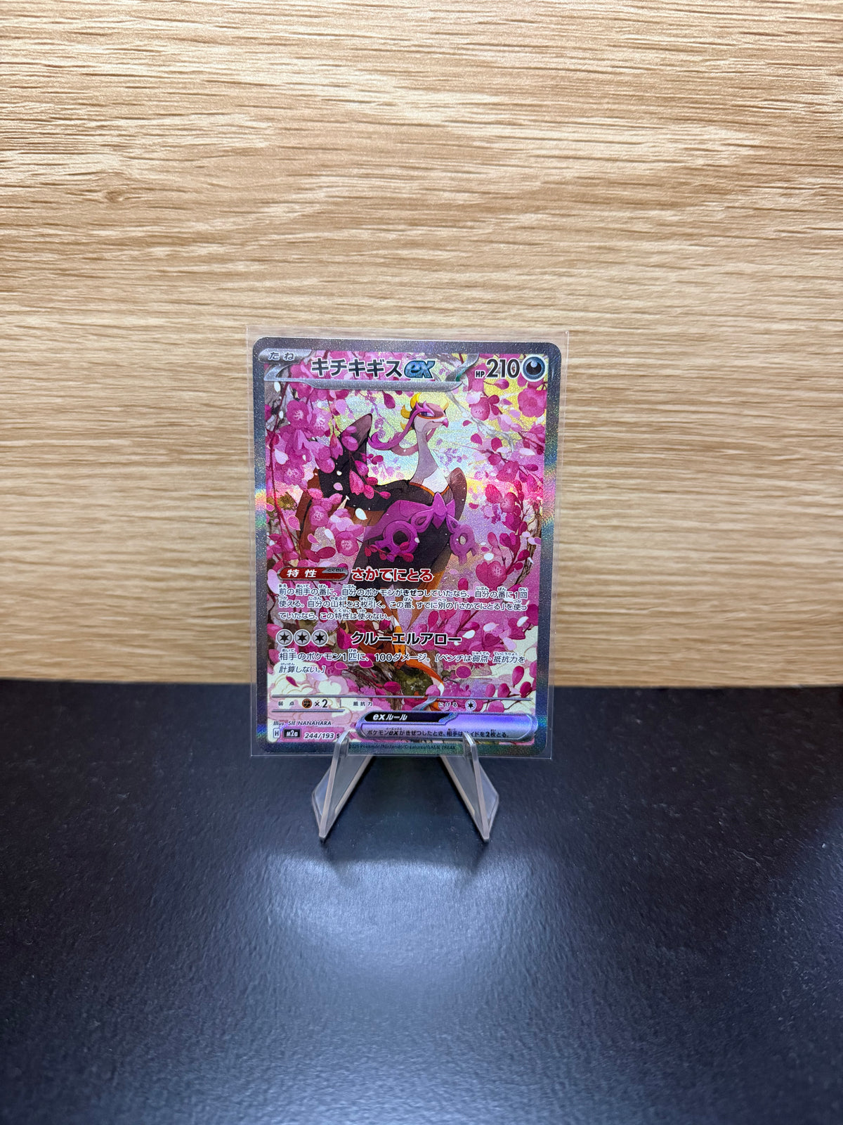 Japanese Fezandipiti ex Pokémon card displayed on a stand