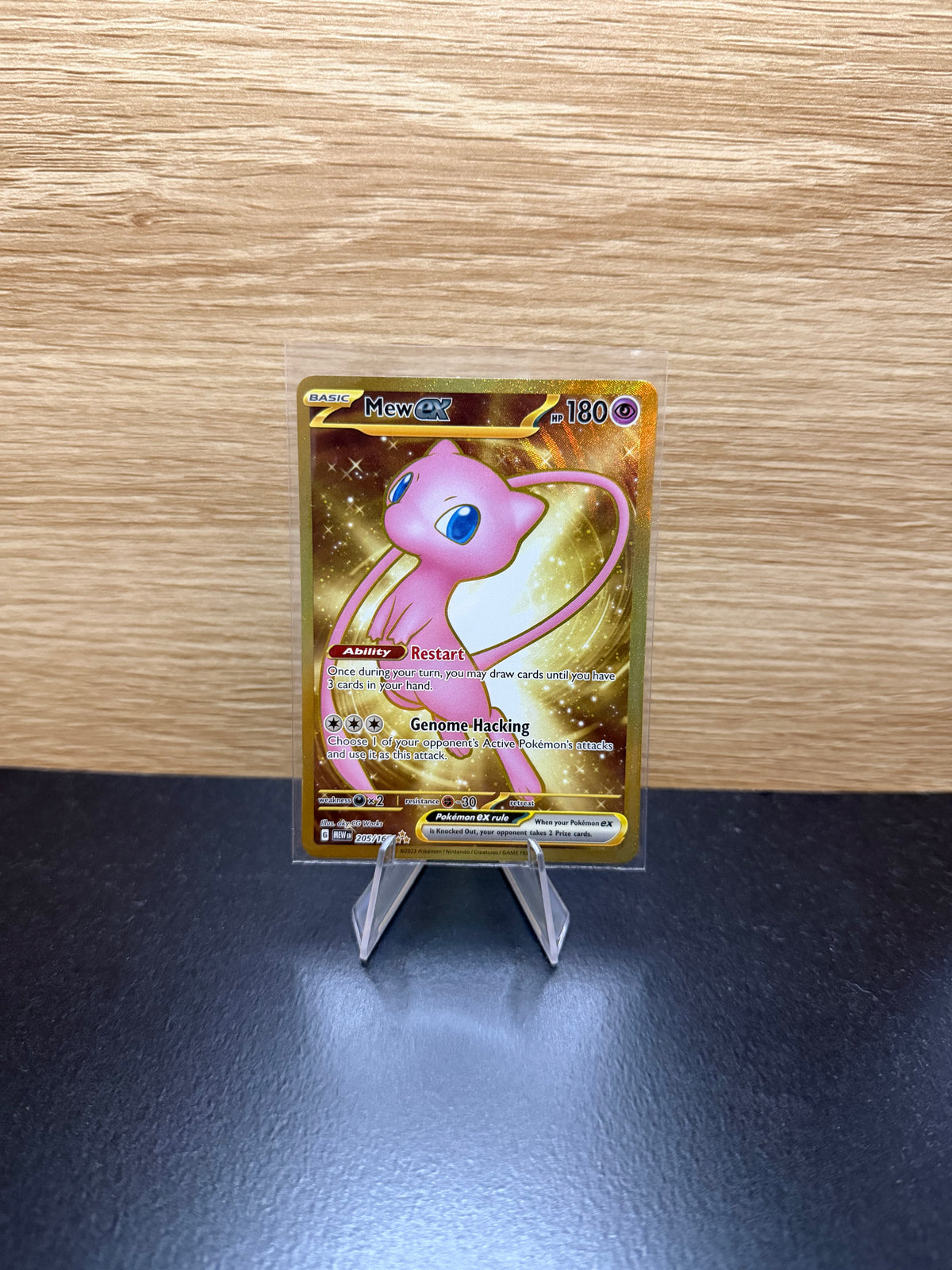 English Mew ex Pokémon card with gold artwork displayed on a stand